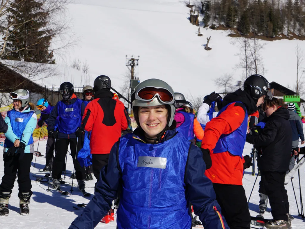 Jugendliche mit Helm und Skibrille am Pistenrand.